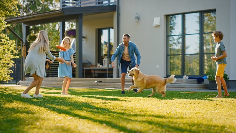 Smiling beautiful family of four play fetch flying disc with happy golden retriever dog on the backyard lawn